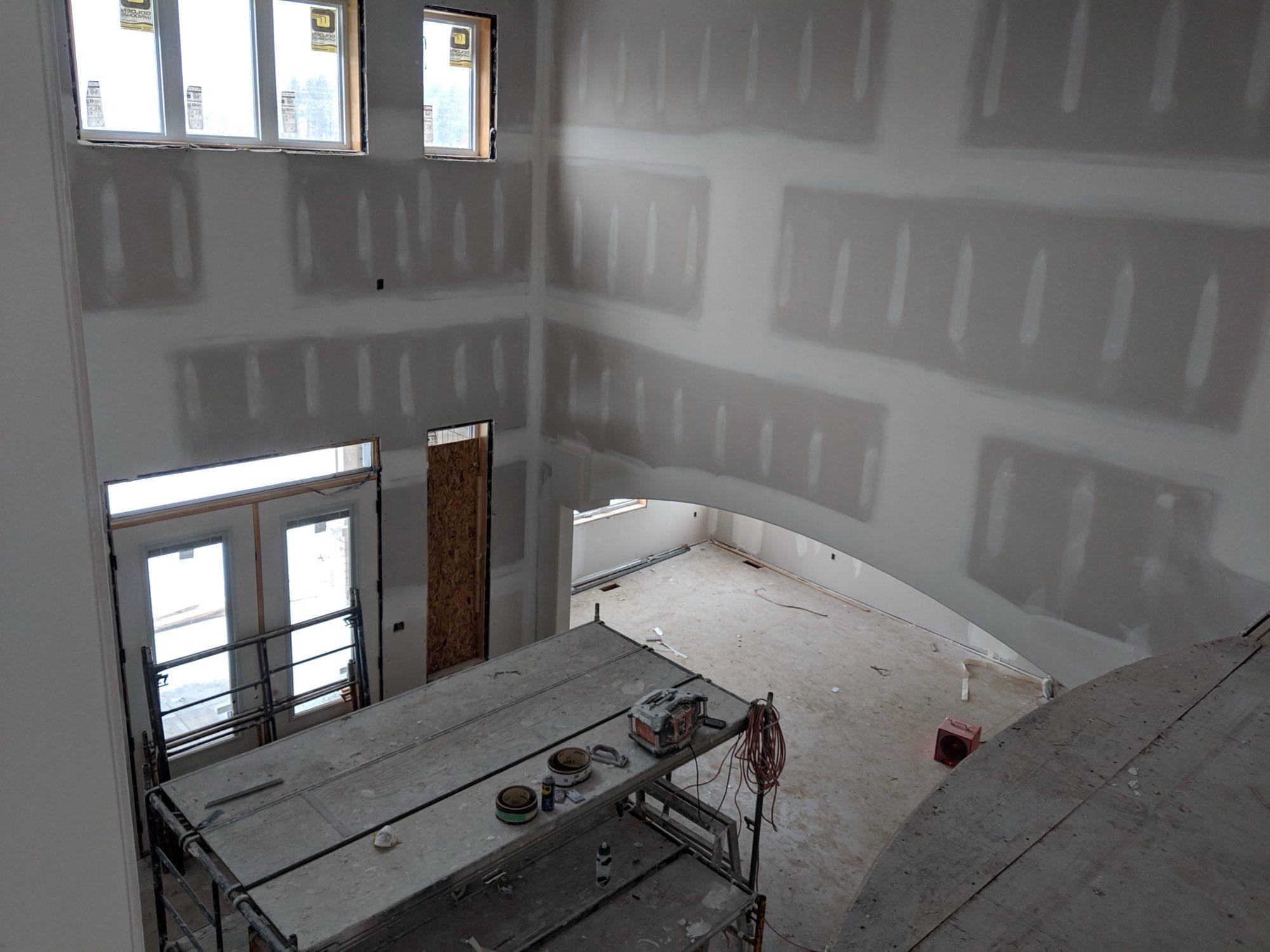 A two-storey room boarded and taped, with scaffolding and a work table still standing on the subfloor