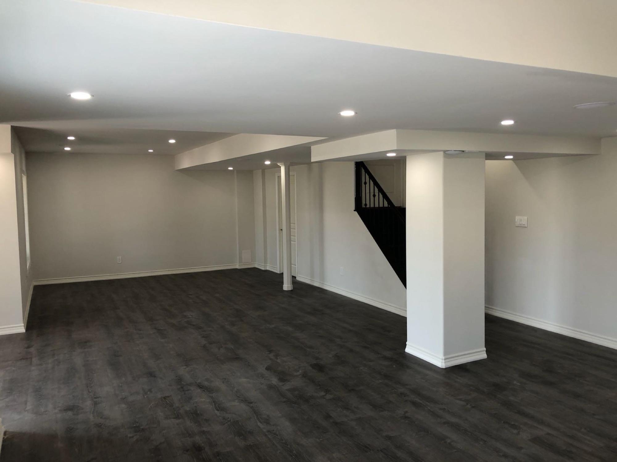 A finished basement in dark plank flooring, with a boxed steel post and a railed staircase up to the main floor — project photo 40